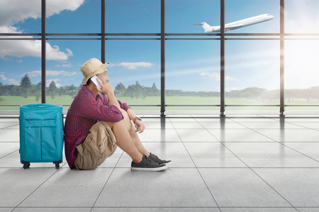 Side view of asian man sitting and talking on cellphone while waiting plane on airport terminalの写真素材