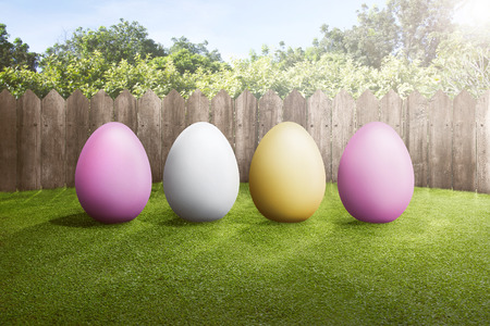 Row of colorful easter eggs on green grass with wooden fence backgroundの写真素材