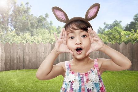 Happy asian little child with bunny ears with wooden fence backgroundの写真素材