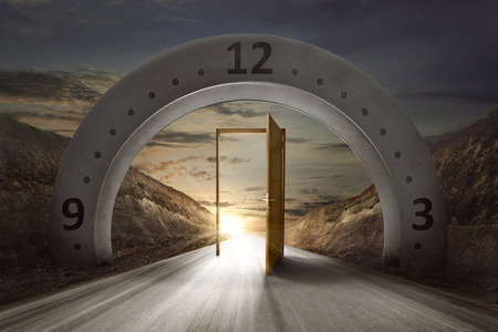 Gateway arch with clock face and open door on the empty road. Daylight Savings Time Conceptの写真素材