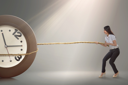 Pretty asian businesswoman pulling a clock with rope over gray backgroundの写真素材