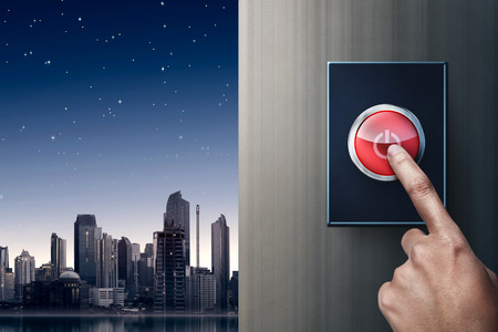 Hand turning off switch on the wall with city at night backgroundの写真素材