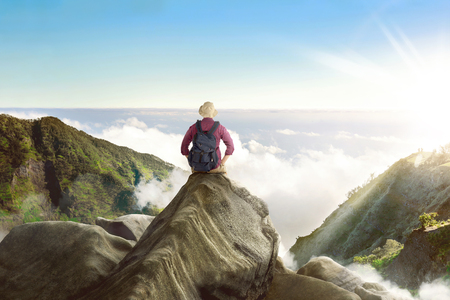 Back view of asian backpacker sitting and enjoying panorama from the cliffの写真素材