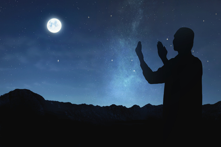 Silhouette of muslim man raising hand and praying to god at nightの写真素材