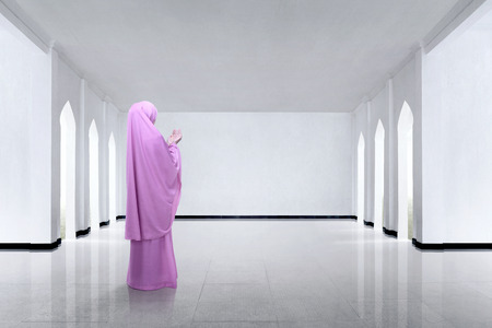 Back view of asian muslim woman raising hand and praying on the mosqueの写真素材