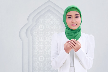 Smiling asian muslim woman raising hand and pray with white wall backgroundの写真素材