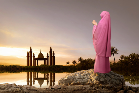Rear view of asian muslim woman with headscarf praying during sunset backgroundの写真素材