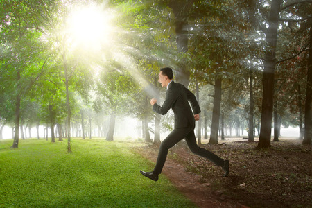 Happy asian businessman running on summer field on sunny dayの写真素材