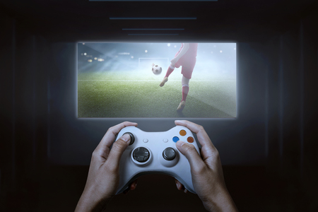 Hands with game controller playing football video game on tvの写真素材