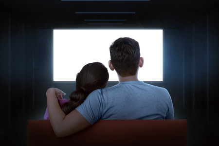 Portrait of asian couple sitting on couch watching blank tv at homeの写真素材