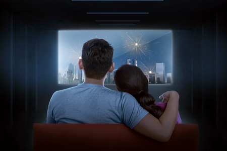 Rear view of asian couple watching celebration on tv at dark roomの写真素材
