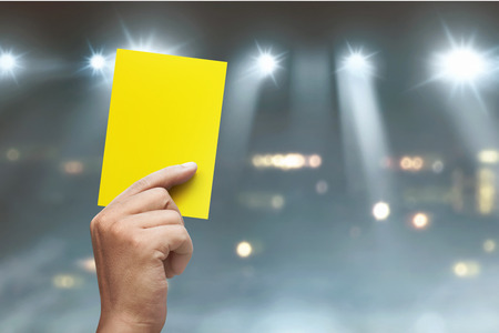Hand of referee with yellow card on soccer stadium at matchの写真素材