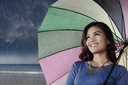 Smiling asian woman with umbrella enjoying rainy day at outdoorの写真素材