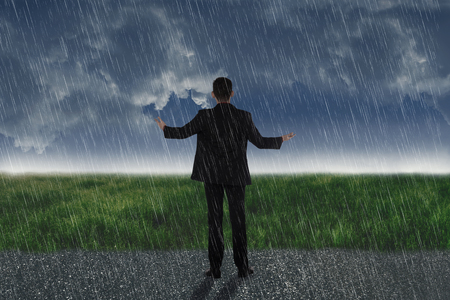 Rear view of asian businessman standing on the rain with dark sky backgroundの写真素材