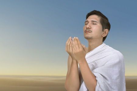 Young asian muslim man praying to god over blue sky backgroundの写真素材