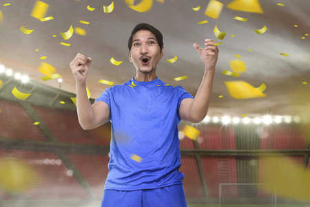 Joyful asian football player man with excited expression on stadium の写真素材