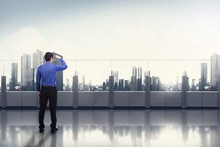 Young asian businessman looking at the cityscape from office terraceの写真素材