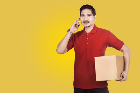 Professional asian delivery man using phone while carrying parcel over colored background