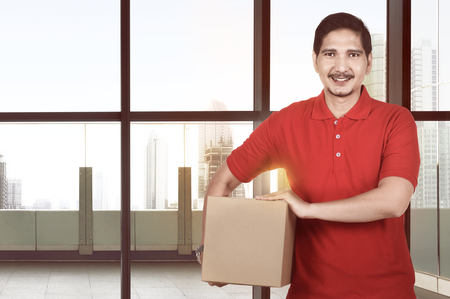 Attractive asian delivery man carrying package on the officeの写真素材