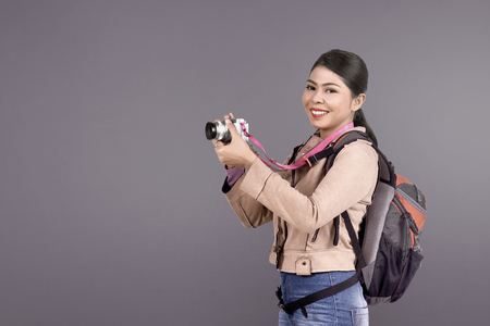 Cheerful asian traveler woman taking a photos with camera over colored backgroundの写真素材