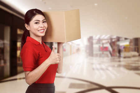 Smiling asian courier woman carrying the parcel to deliverの写真素材