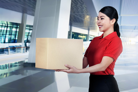 Beautiful asian courier woman bring the parcel on the office buildingの写真素材