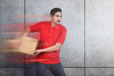 Attractive asian male courier bring the box with wall backgroundの写真素材