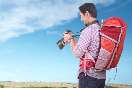 Handsome asian tourist with backpack holding camera with blue sky backgroundの写真素材