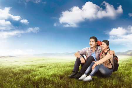 Romantic asian backpacker couple sitting and enjoying the view at meadow の写真素材