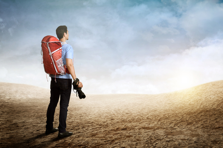 Back view of asian backpacker man holding camera on the mountainの写真素材