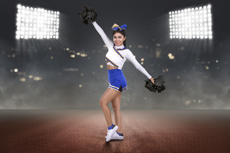 Happy asian cheerleader performing with poms on the stadiumの写真素材