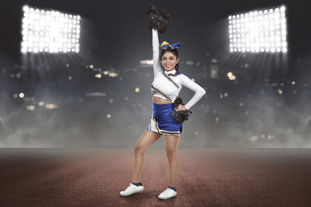 Young asian cheerleader action with pom-poms on the stadiumの写真素材