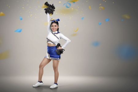 Happy asian cheerleader with pom-poms in her hands over confetti backgroundの写真素材
