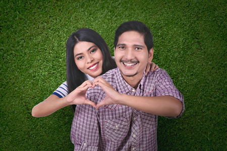 Happy asian couple in love make a heart shape with hands over green backgroundの写真素材