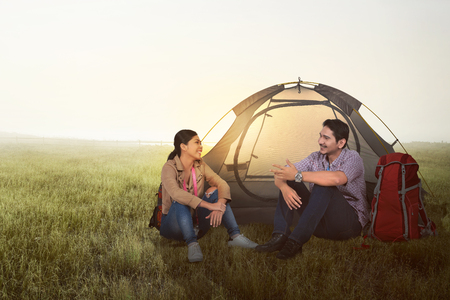 Smiling asian couple camping with backpack and tent on the meadow fieldの写真素材