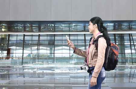 Smiling asian tourist woman with backpack using cellphone on the airportの写真素材