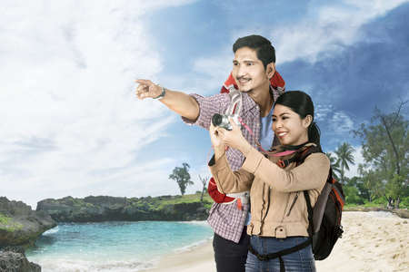 Joyful asian couple traveler sightseeing and taking a photos on the beachの写真素材