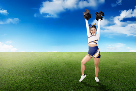 Cute asian cheerleader holding pom poms in her hands on the fieldの写真素材