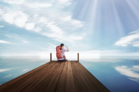 Attractive asian traveler man sitting and enjoying view from the dockの写真素材