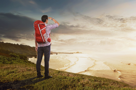 Rear view of asian traveler man with backpack looking at panorama from cliffの写真素材