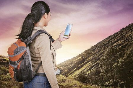 Attractive asian traveler woman with backpack using mobile phone on the mountainの写真素材