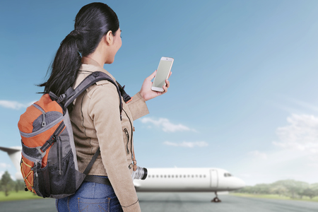 Happy asian tourist woman with phone going traveling with airplane on the backgroundの写真素材