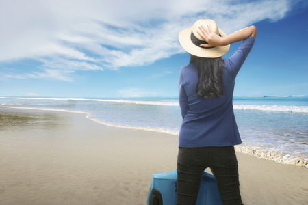 Rear view of asian traveler woman with suitcase relaxing on the beachの写真素材