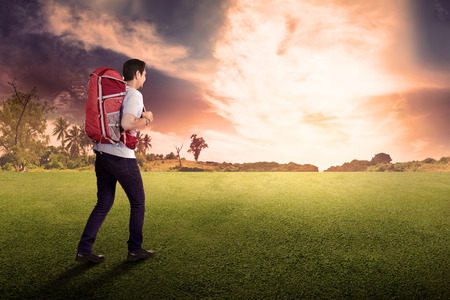 Rear view of asian man traveler with backpack on the field at sunsetの写真素材
