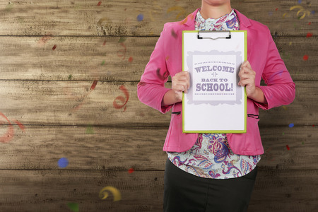 Woman teacher holding clipboard with welcome back to school message over wooden wall background