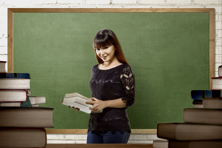 Pretty asian university student woman holding books on the classの写真素材