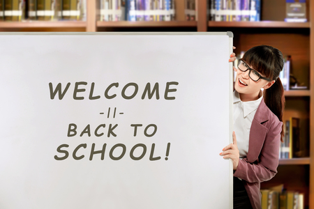 Pretty asian female teacher with Welcome back to school message on the whiteboard