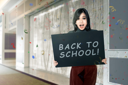 Happy asian student woman with board with back to school text on the corridor