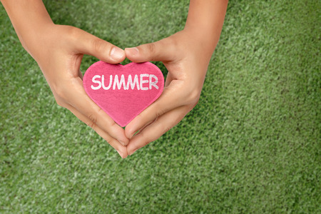 Hands holding red heart with Summer text over green grass backgroundの写真素材