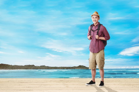 Handsome asian tourist man with backpack standing against ocean view backgroundの写真素材